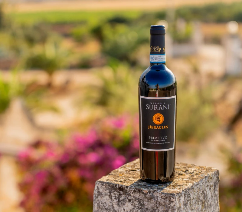 Bottiglia Hèracles Primitivo di Manduria Surani su sfondo masseria